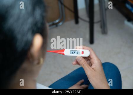 A woman is holding a thermometer and the temperature is 35.2. The woman is sitting on the floor Stock Photo