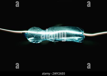A crushed plastic bottle partially filled with water, lying horizontally on a black background with a black artificial carpet. The bottle is illuminat Stock Photo