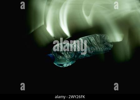 A crushed plastic bottle partially filled with water, lying horizontally on a black background at a 45-degree angle with the screw cap facing the came Stock Photo