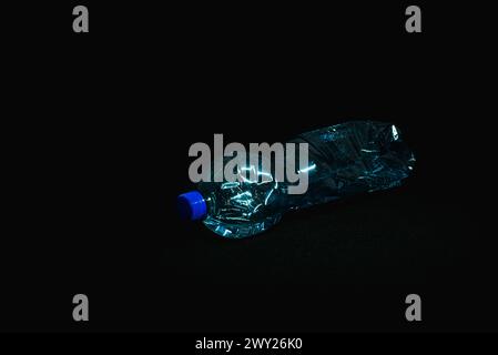 A crushed plastic bottle partially filled with water, lying horizontally on a black background at a 45-degree angle with the screw cap facing the came Stock Photo