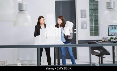 Specialists examine 3D models to decide on measurements while developing small business growth ideas. Team of architects construct floor plan strategy with industrial scale dimensions. Stock Photo