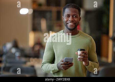 Portrait of smiling African American man holding paper cup with coffee and smartphone in office cafe copy space Stock Photo