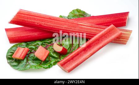 Red rhubarb stems' cuts over rhubarb leaves isolated on white background. Stock Photo