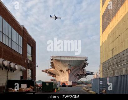 A passenger jet descends into Philadelphia International Airport above the U.S.S. John F. Kennedy at dock in the Philadelphia Navy Yard. Stock Photo