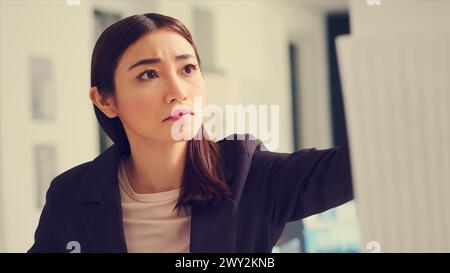 Asian architect examines industrial blueprints and maquette to calculate real measurements and lines dimension. Technician looking at 3D building model and analyzing layout sketch. Handheld shot. Stock Photo