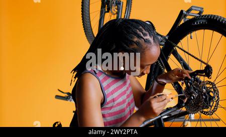 Close up of engineer using screwdriver and hex socket wrench to secure wheel on bicycle in studio background. Professional screwing bolts on bike parts, mending rear derailleur and cassette, camera B Stock Photo
