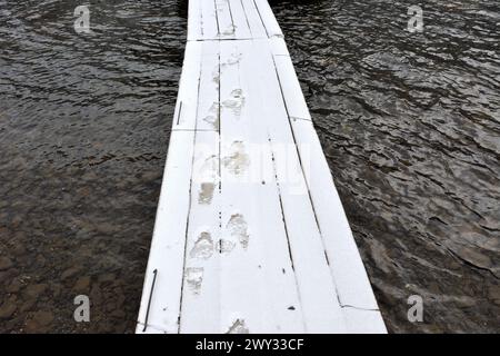 Human footprints on a snow-covered wooden platform above the calm water of a mountain lake. Lake Kok-Kol, Altai, Siberia, Russia. Stock Photo