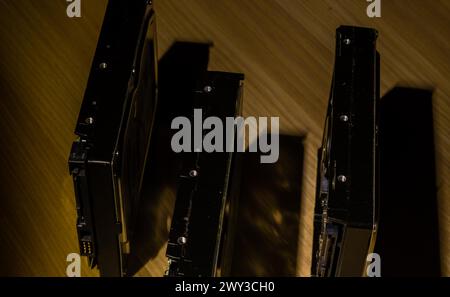 Three desktop computer hard disk drives on wooden workbench in soft light casting shadows Stock Photo