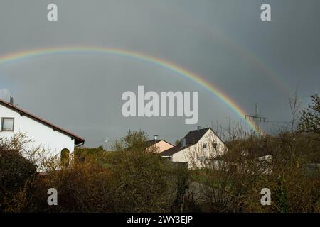 Rainbow over houses and electricity pylons against a blue sky Stock Photo