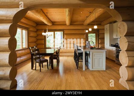 Dark brown stained wooden table with upholstered seat high back chairs and white painted island with bar stools in open concept dining room and Stock Photo