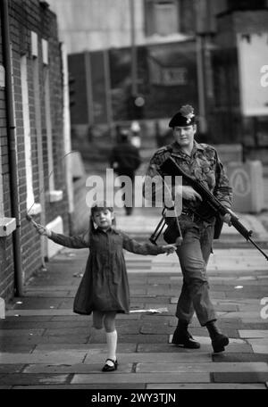 Ireland The Troubles daily life  Belfast 1980s. Girl skipping with British Army soldier patrolling the streets. 1981 UK HOMER SYKES Stock Photo