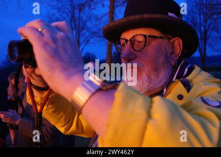 Older male vlogger in hat films the Easter bonfire. His face is lit red by the fire Stock Photo