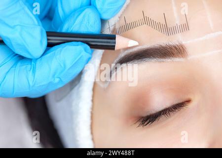 Permanent make-up for eyebrows of beautiful woman with thick brows in beauty salon. Closeup beautician doing  tattooing eyebrow. Stock Photo