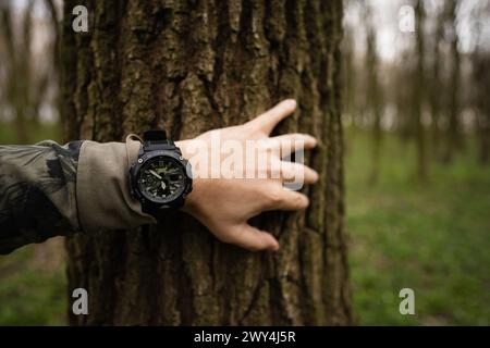 Ternopil, Ukraine- April, 2023: A close-up image depicting a hand with a black tactical watch G-Shock touching a tree trunk in a forest setting, empha Stock Photo