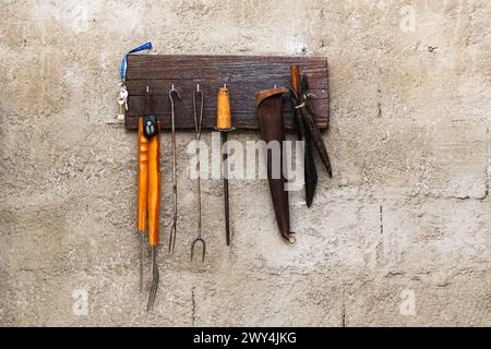 A collection of tools hanging on a wall. The tools include a hammer, a pair of pliers, a screwdriver, and a wrench. The wall is made of concrete and h Stock Photo