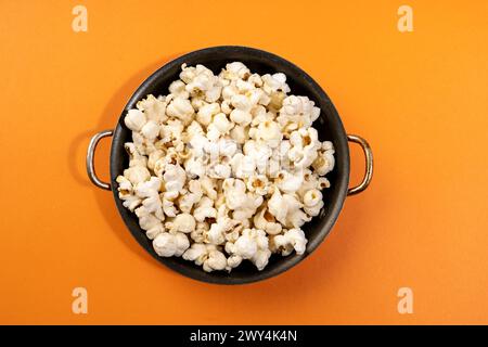 An orange background with a black bowl of popcorn. Stock Photo