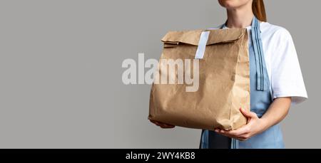 Waitress holds brown package bag for takeout food in her hands. Takeaway food online order. Stock Photo