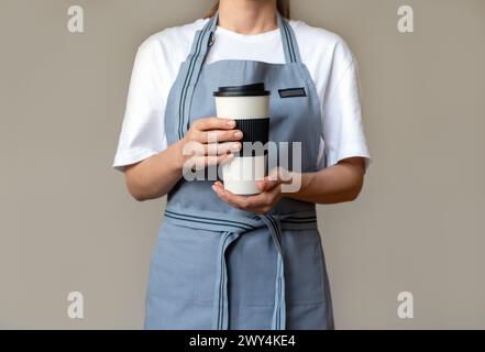 Waitress wearing apron holding in her hands compostable paper travel coffee cup with compostable lid. Natural plant fibre materials for disposable cup Stock Photo