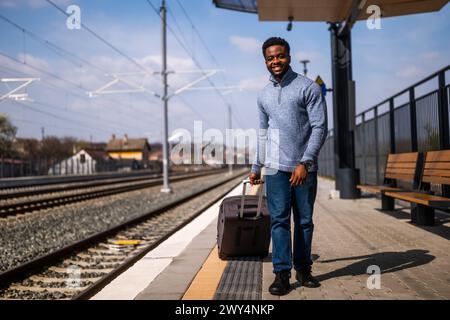 Happy man with suitcase walking on railway station. Stock Photo