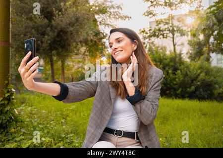 Young caucasian woman taking a selfie with cell phone and smiling outdoors. Stock Photo