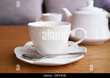 White cup with tea being steeped in a teapot in the backdrop Stock Photo