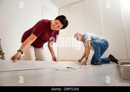 Senior couple installing laminate flooring in their new home together. DIY concept. Mature woman and man doing renovation. Stock Photo