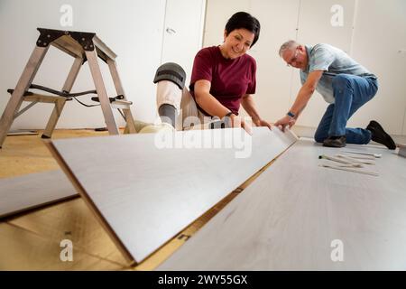 Senior couple installing laminate flooring in their new home together. DIY concept. Mature woman and man doing renovation. Stock Photo