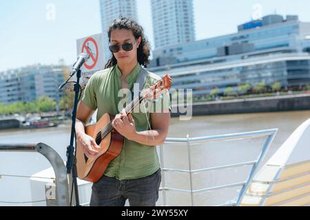 young latin man with long hair and busker glasses guitarist in Buenos Aires, working making art and street music with his guitar, copy space. Stock Photo