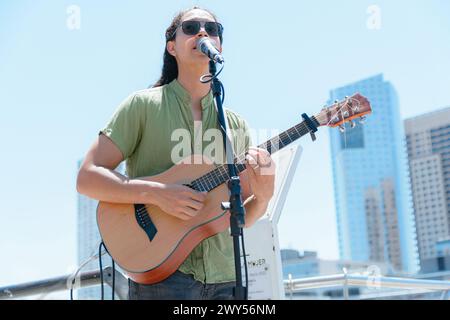 young latin man with long hair and busker glasses guitarist in Buenos Aires, working making art and street music with his guitar, copy space. Stock Photo