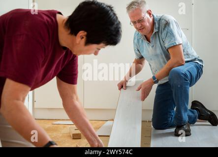 Senior couple installing laminate flooring in their new home together. DIY concept. Mature woman and man doing renovation. Stock Photo