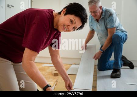 Senior couple installing laminate flooring in their new home together. DIY concept. Mature woman and man doing renovation. Stock Photo