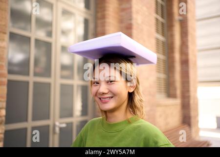 Portrait of young smiling Chinese student sitting on a bench on campus looking at the camera Stock Photo