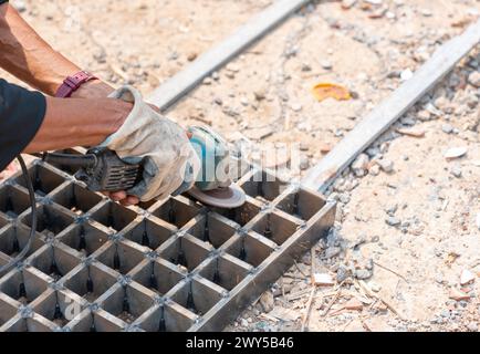 Worker cutting or grinding power tools for a finished metal grate construction frame in a metal workshop. Stock Photo
