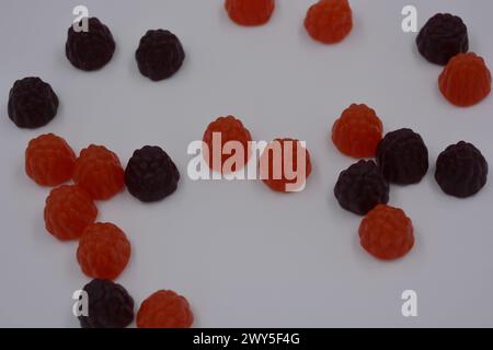 Unusual sweets, colored jelly candies in the form of fruits. Red, black jelly blackberry, raspberry are arranged on a white background. Stock Photo