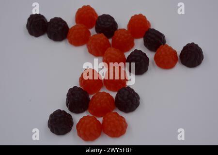 Unusual sweets, colored jelly candies in the form of fruits. Red, black jelly blackberry, raspberry are arranged on a white background. Stock Photo