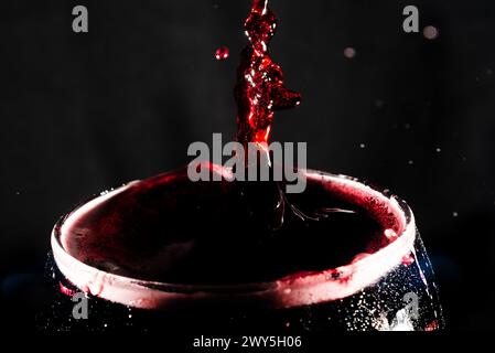 Close-up of the top of a clear glass goblet filled with wine with splashes of water. Splash Effect. Isolated on dark background. Stock Photo