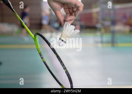 The badminton player holding a white shuttlecock and racket and standing at the net ready to serve. Stock Photo