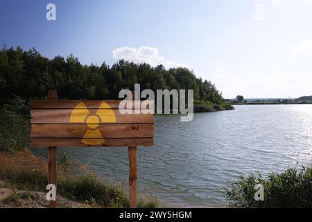 Radioactive pollution. Yellow warning sign with hazard symbol near river outdoors Stock Photo