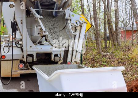 On construction site, wet cement is being discharged from cement truck chute into concrete buggy equipped with wheelbarrow track Stock Photo