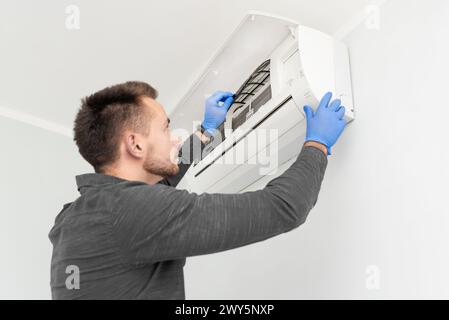 A man is fixing an air conditioner. He is wearing gloves and a blue shirt Stock Photo