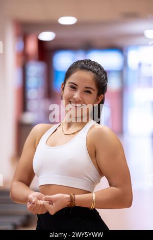 A happy young female athlete poses confidently in her gym attire, ready for her workout, with exercise equipment blurred in the background.  Stock Photo