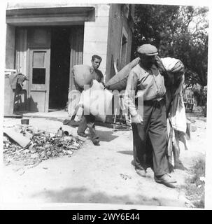 A FRENCH FAMILY RETURN TO THEIR SHELL TORN VILLAGE - M. Mathurin Le Du and Rene carry out bedding from the house of M. Renoulf for airing. , British Army, 21st Army Group Stock Photo