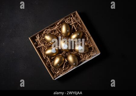 Gold eggs in paper box on black background. Top view. Stock Photo