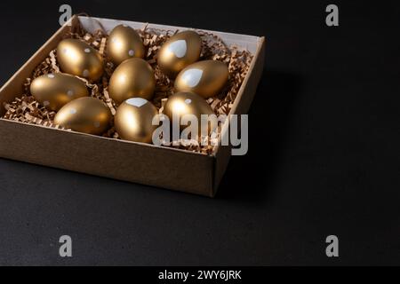 Gold eggs in paper box on black background. Stock Photo