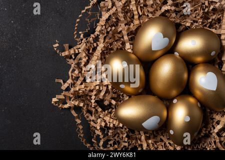Golden eggs in paper nest on dark table. Stock Photo