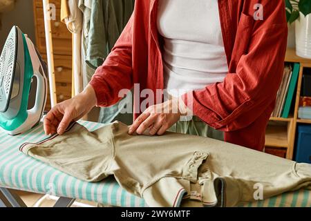 Unrecognizable  middle aged woman ironing washed clothes on ironing board at home. Housewife daily routine. Housekeeping concept. Stock Photo