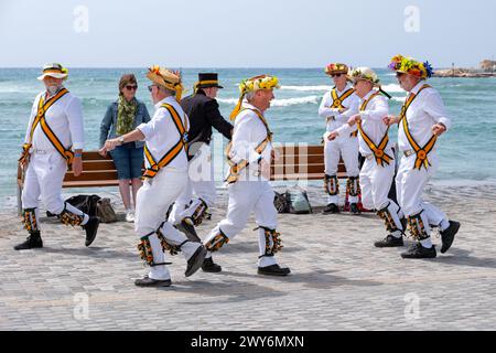 A group of touring British morris men or dancers dancing in the Old Harbour area of Paphos, Cyprus. the group are dressed in white with straw hats Stock Photo