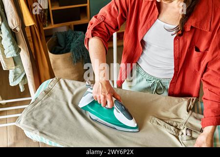 Unrecognizable middle aged woman ironing washed clothes on ironing board at home. Housewife daily routine. Housekeeping concept. Stock Photo