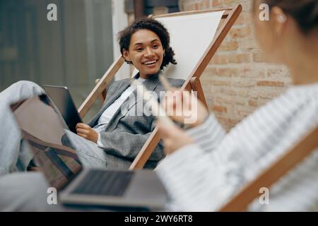 Two young female colleagues discussing a new project while sitting at office terrace Stock Photo