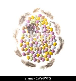Pastel coloured sugar-coated mini eggs arranged in an egg shape edged with feathers on a white background. Stock Photo